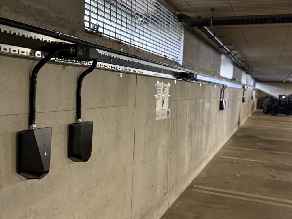 Black EV chargers mounted along a concrete wall in the underground car park at Tulip Court, Alpine Place, fed from an overhead busbar running the length of the bay.